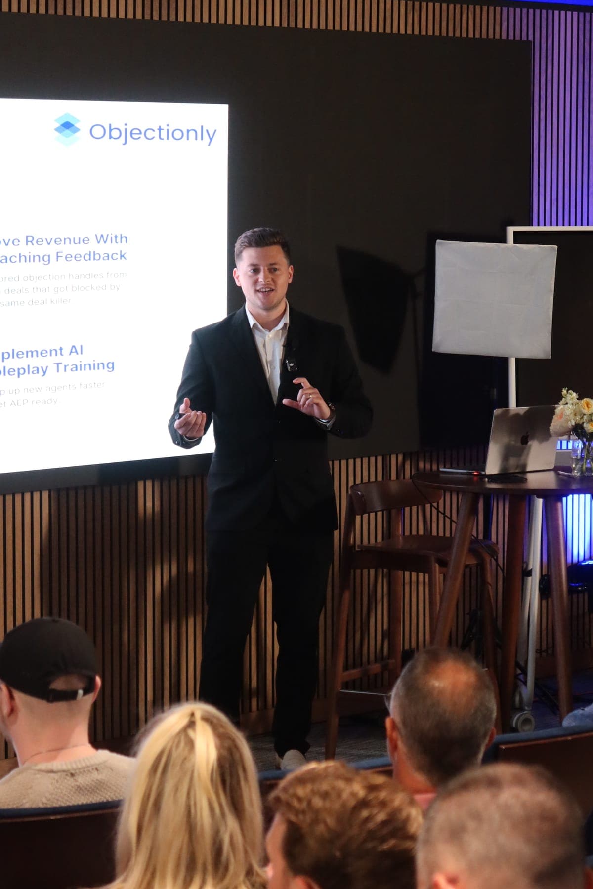 A talk on Objectionly in front of a seated audience, with slides on coaching feedback and AI roleplay training